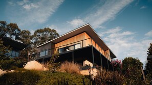 Une maison moderne à deux étages, dotée d’un toit plat, de grandes fenêtres et d’un balcon.