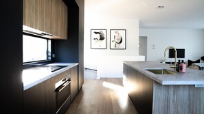 Una cocina moderna con una isla grande, armarios oscuros y un ventanal que proporciona luz natural.