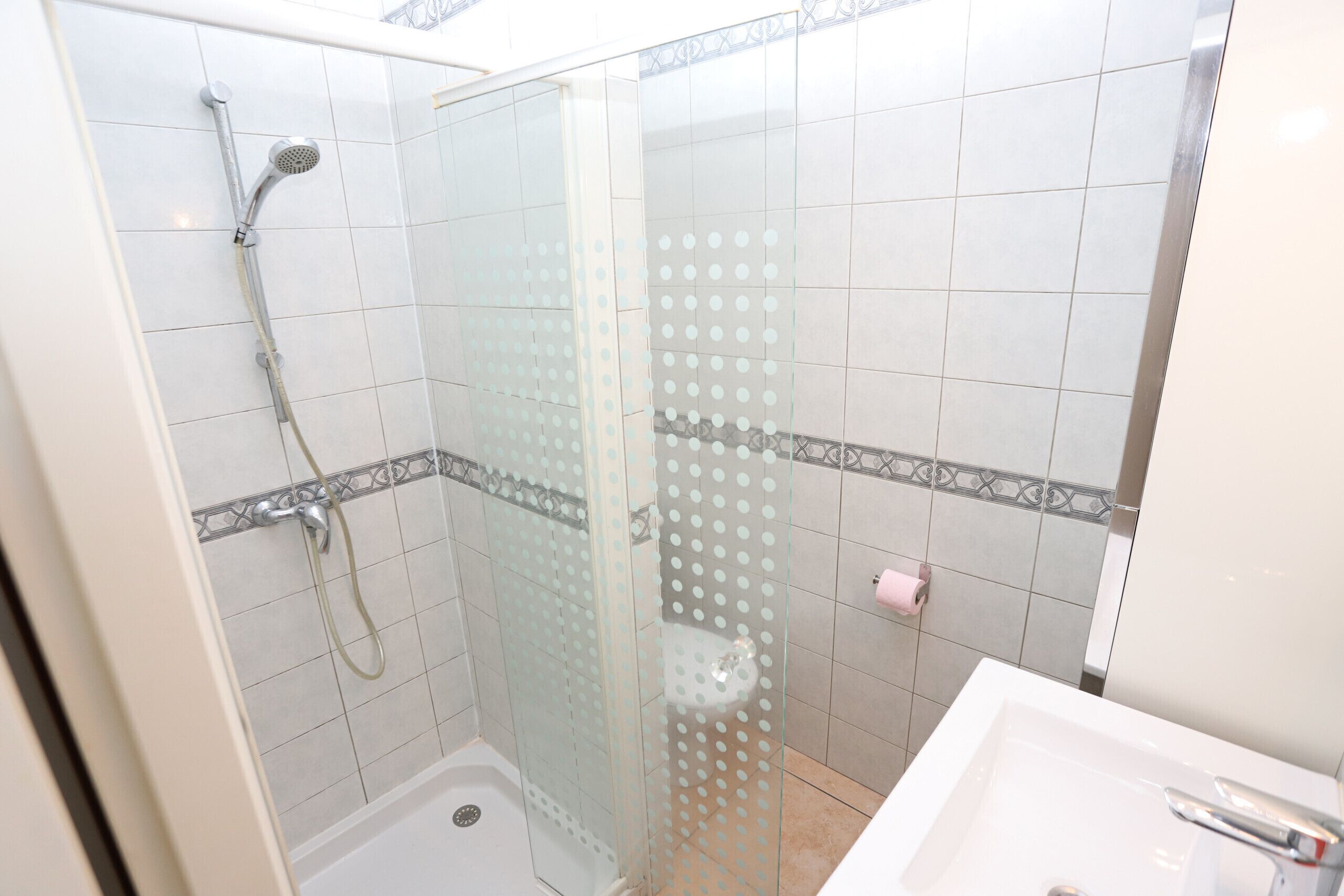 A shower with a glass door, a white bathtub, and a sink with a mirror.