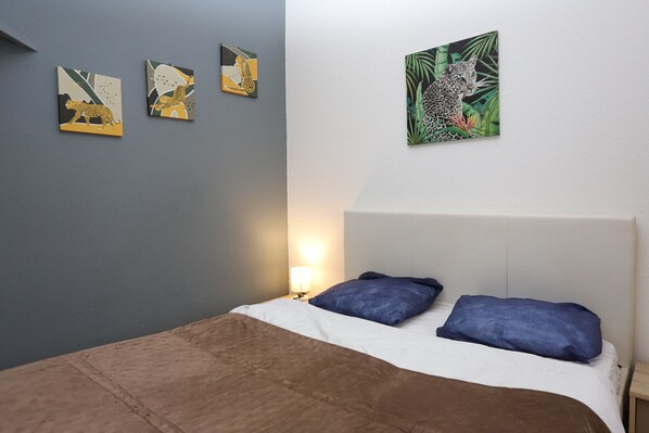 A bedroom with a bed, two pillows, a nightstand, a lamp, and three leopard-themed wall art pieces.
