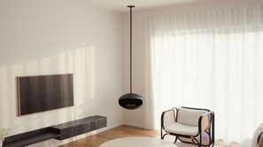 A modern living room with a flat-screen TV mounted on the wall, a black pendant light, a wooden floor, and a window with sheer curtains.