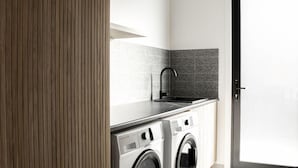 Une petite buanderie comprenant un lave-linge, un évier et une porte.