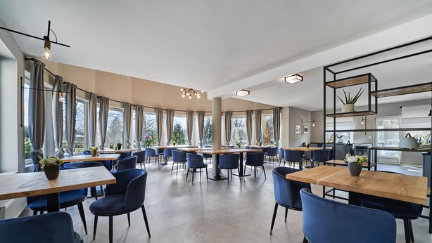A spacious dining area with multiple tables and chairs, large windows, and a modern chandelier. - Hotel Arborétum (Harkany)
