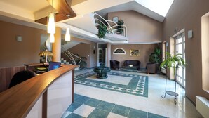 A spacious lobby with a high ceiling, a central fountain, and a staircase leading to an upper level. - Hotel Arborétum (Harkany)