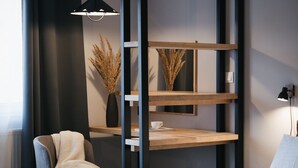 A modern hotel room with a bed, a chair, a shelf unit, and a vase with dried plants. - Hotel Arborétum (Harkany)