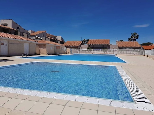 A swimming pool with a tiled deck, surrounded by buildings with red-tiled roofs.