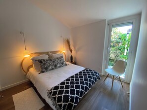 A bedroom with a bed, bedside lamps, a chair, and a view of greenery outside.