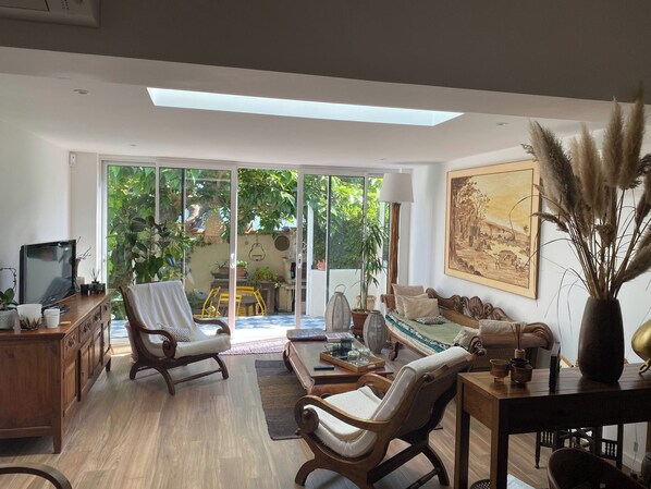 A spacious living room with a large sliding glass door leading to a garden, a wooden coffee table, and a comfortable seating area with sofas and chairs.