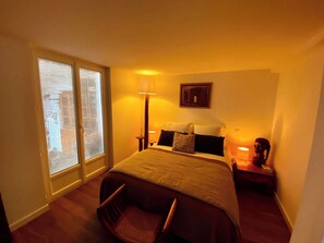 A hotel room with a large bed, a chair, a nightstand, a lamp, and a window with a view of buildings. - Villa flower district 5 min walk from the beaches à Canet En Roussillon (Canet-en-Roussillon)