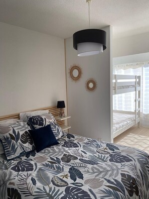 A bedroom with a bed, a bedside table, a lamp, a bunk bed, and wall decorations.