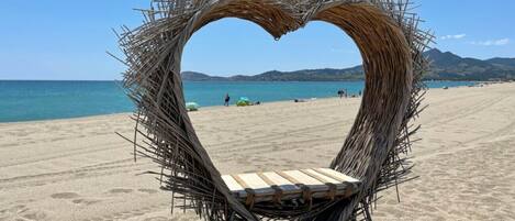 A beach with a heart-shaped structure made of sticks and a wooden bench.