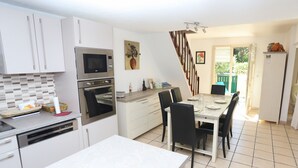 Una cocina moderna con electrodomésticos integrados, un comedor con mesa y sillas, y una escalera que conduce a un balcón.