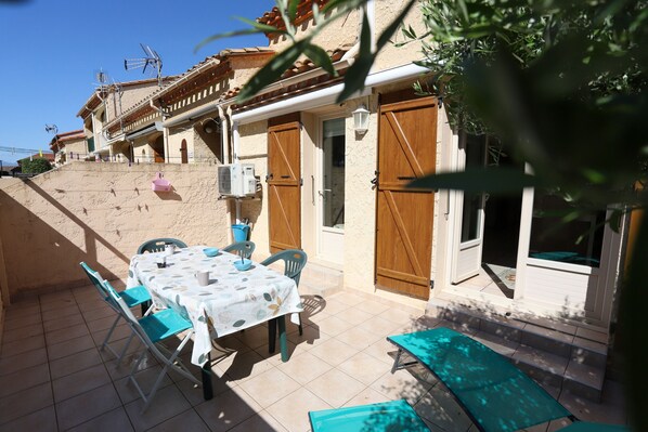 Un patio con una mesa lista para comer, asientos exteriores y una escalera que lleva a un edificio con puertas y ventanas de madera.