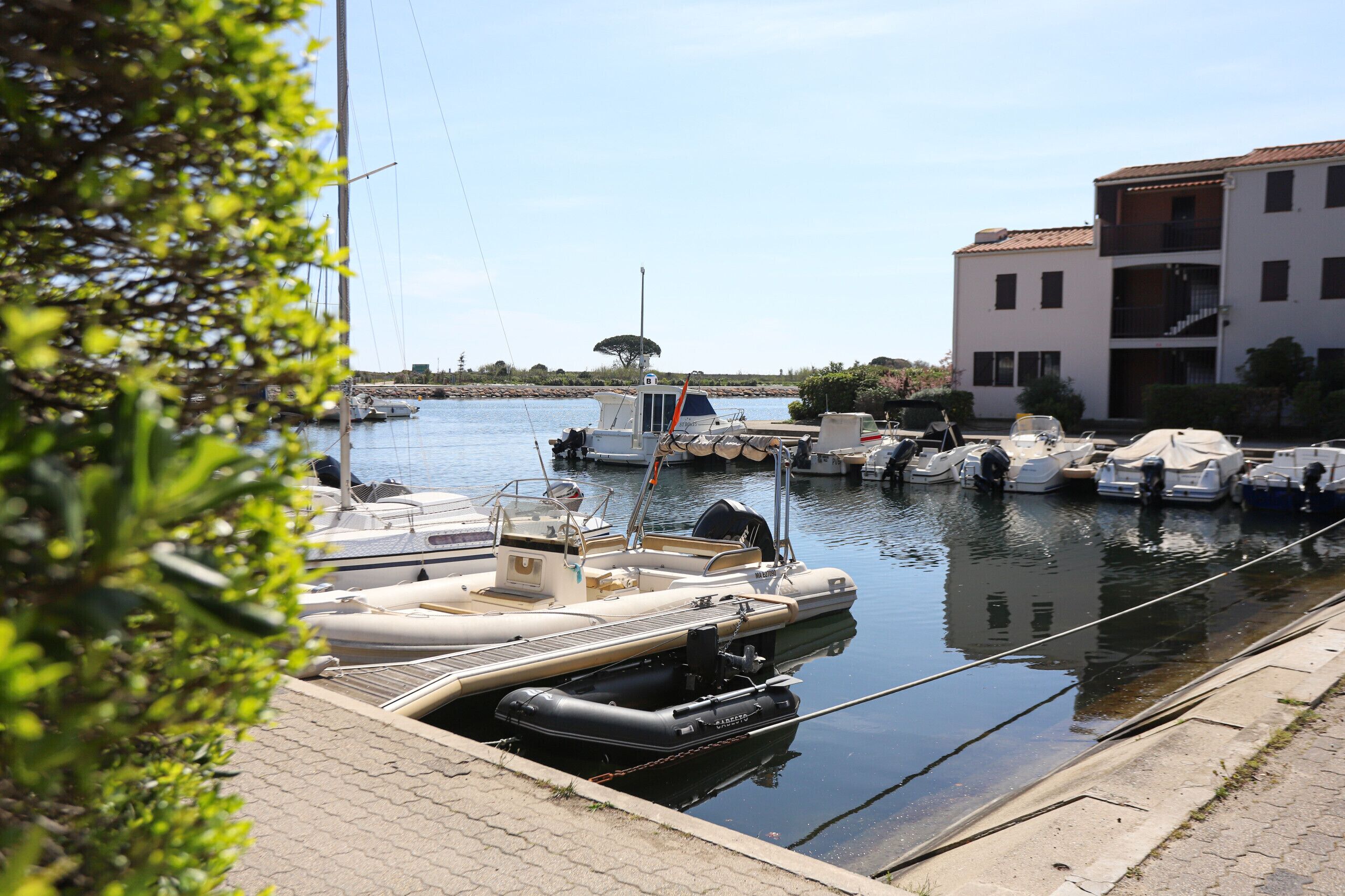 A marina with several boats docked along the water's edge, a building with a balcony, and a clear sky.