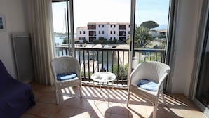 A balcony with two wicker chairs and a small table, overlooking a marina and buildings.