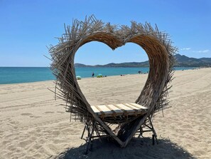 Ein Strand mit einer herzförmigen Konstruktion aus Ästen und einer hölzernen Bank.