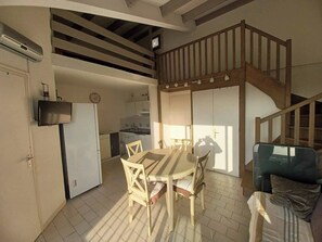 Uma sala ampla com mesa de jantar, cadeiras, sofá e cozinha ao fundo, além de uma escada.