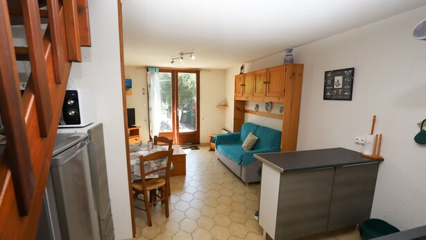 A compact kitchen with a refrigerator, a dining table with chairs, a sofa, and a small cabinet.