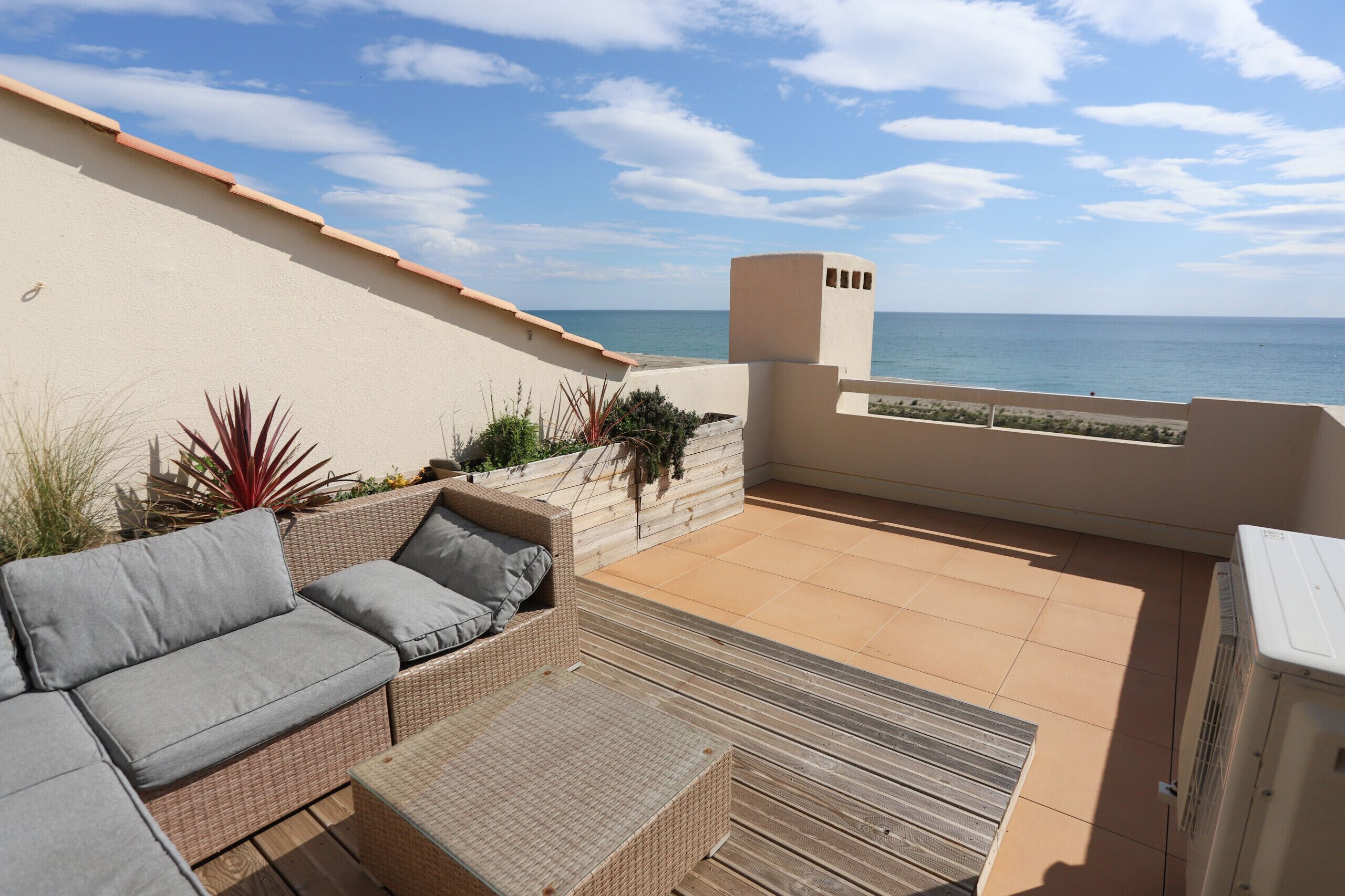 A covered outdoor seating area with a view of the sea, a cushioned sofa, and a small table.