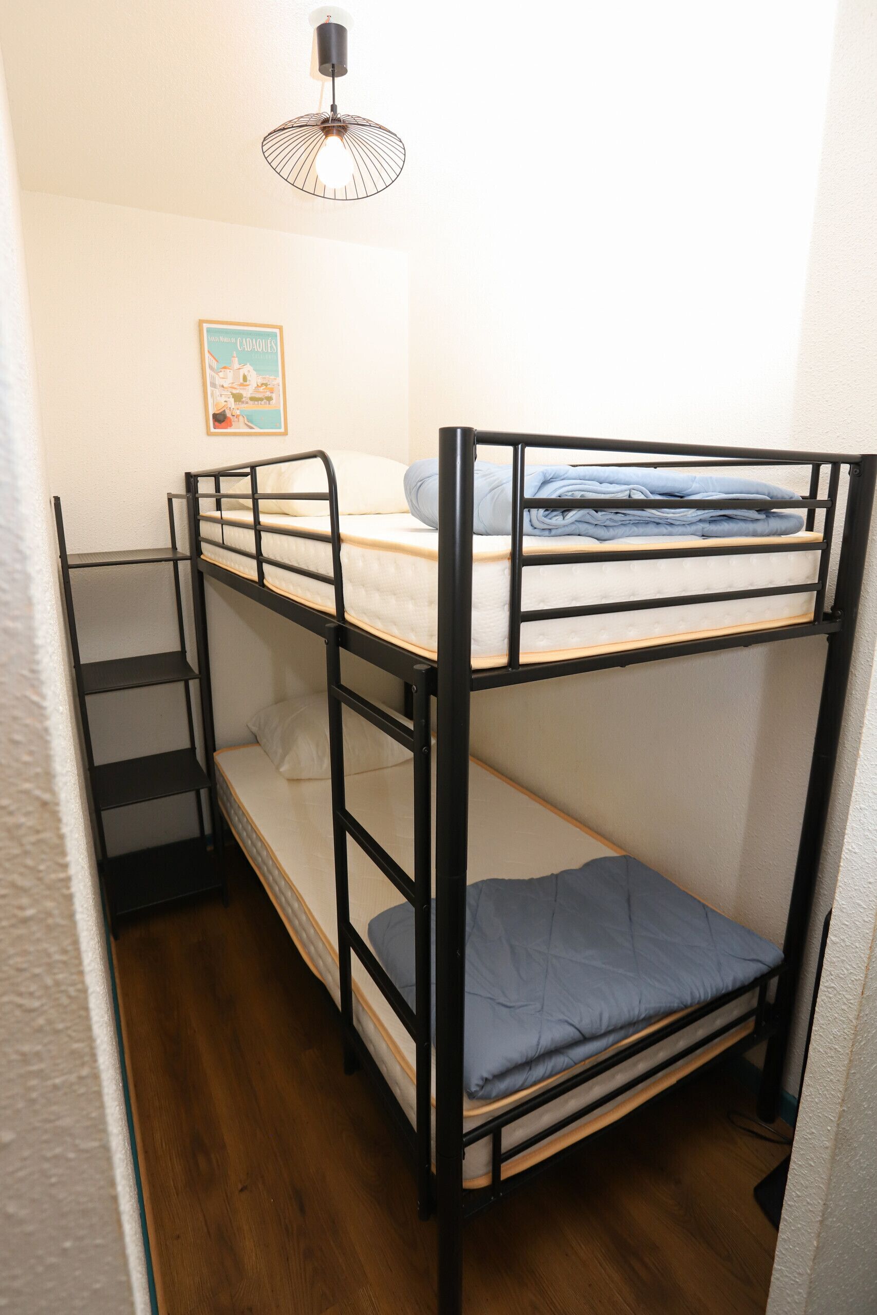 A bunk bed with a mattress and pillows, a small shelf, and a poster on the wall.