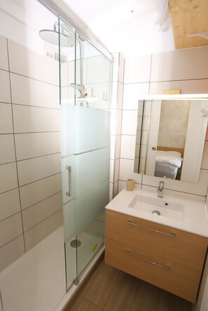 A modern bathroom with a glass-enclosed shower, a white sink with a mirror above it, and wooden cabinetry. - Spacious classified studio with marina,mountain and sea views (Saint-Cyprien)