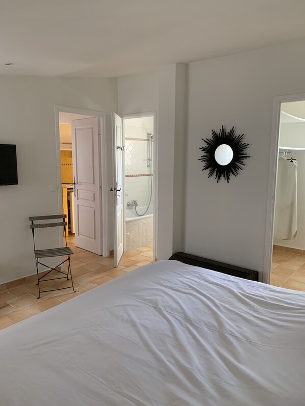 A bedroom with a bed, a chair, a shower, and a mirror on the wall.