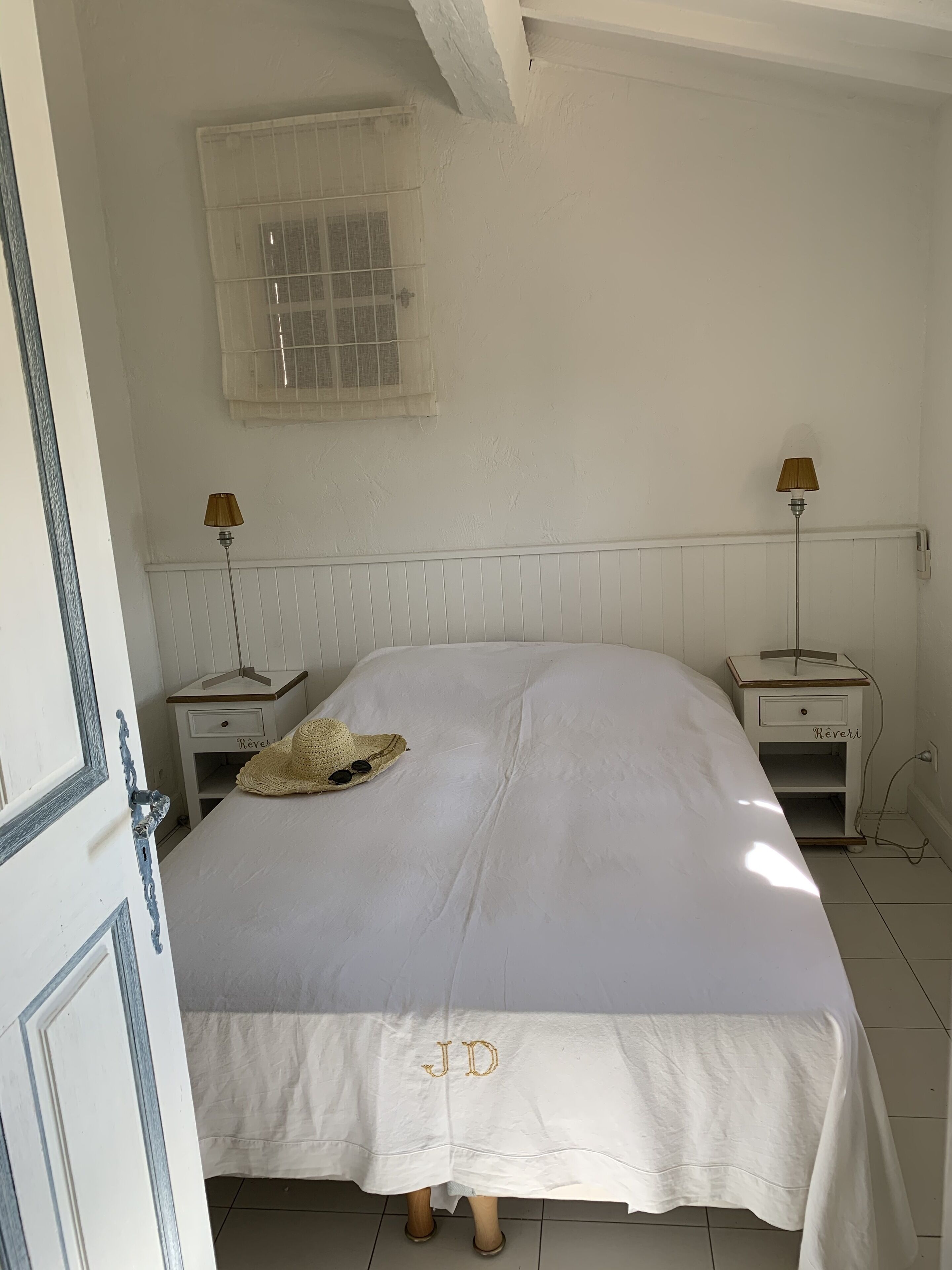 Un dormitorio con una cama, dos mesitas de noche, una lámpara en cada mesita y una ventana con diseño de cuadrícula, además de una puerta.