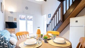 A dining area with a table set for two, a television in the background, and a staircase leading upstairs. - St Cyprien beautiful holiday home near the beach (Saint-Cyprien)