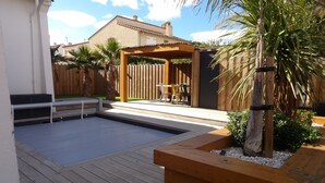 A wooden deck with a pool, a wooden pergola, and a seating area with chairs.