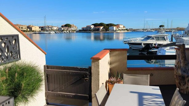 Eine Terrasse mit Tisch und Stühlen mit Blick auf eine Marina, im Hintergrund Boote und Häuser.