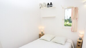 Ein Schlafzimmer mit einem Bett, zwei Nachttischen, einem Fenster mit Vorhängen und einem Regal mit Dekoration.