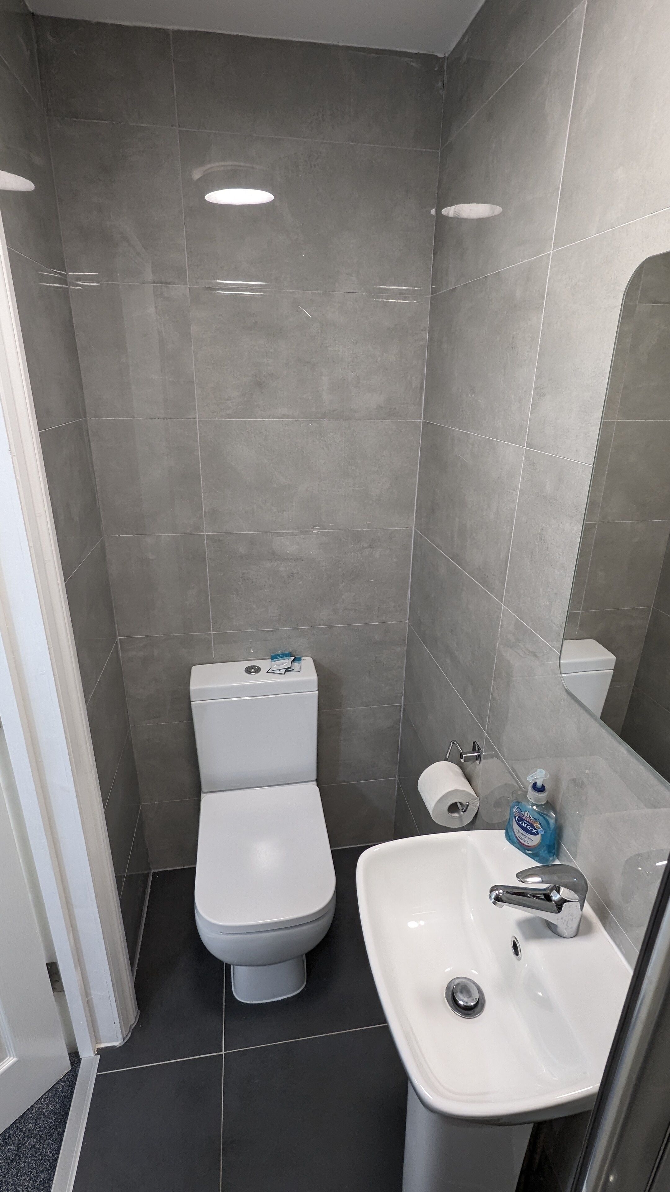 Ein kleines, modernes Badezimmer mit Toilette, Waschbecken und Spiegel.