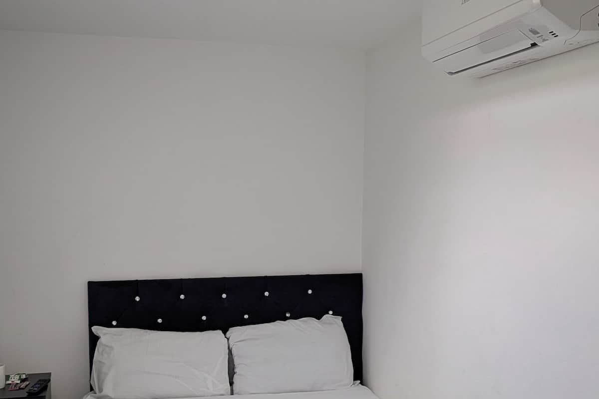 Una cama bien hecha con sábanas blancas, un cabecero oscuro y una unidad de aire acondicionado blanca montada en la pared.