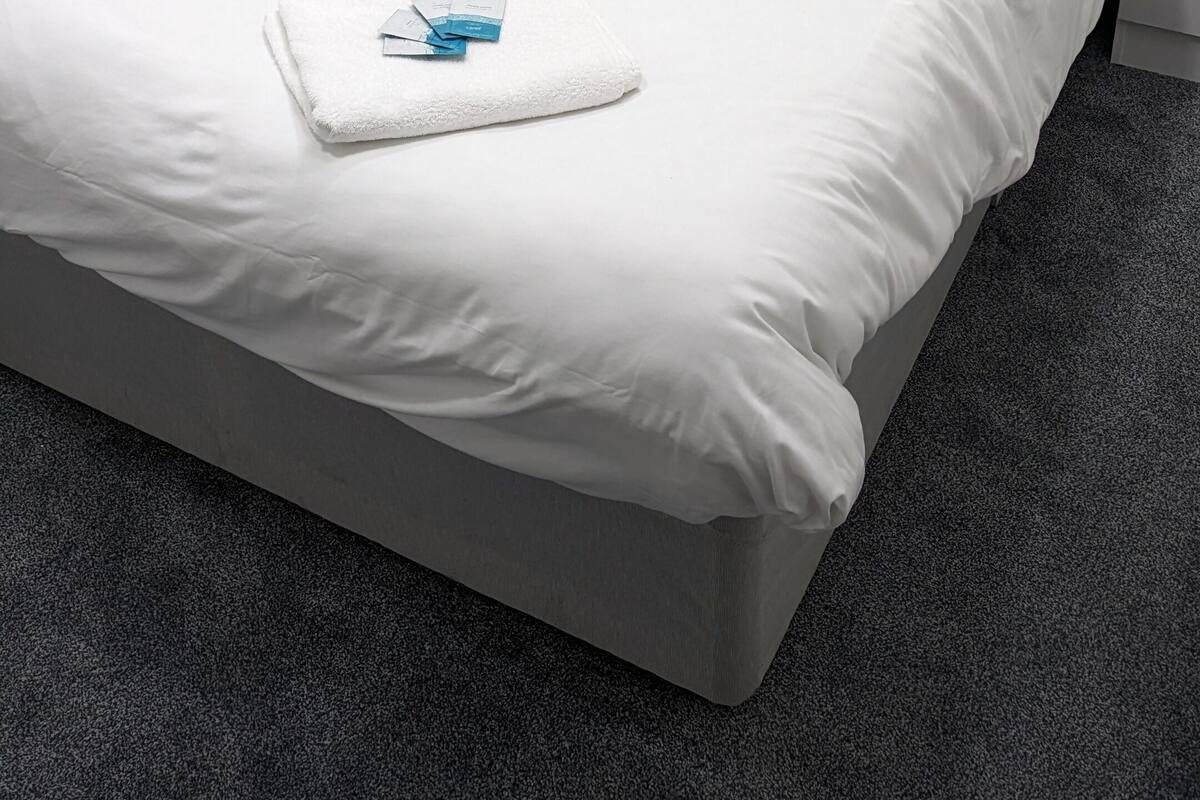 Una cama bien hecha con sábanas y almohadas blancas, una toalla doblada y un objeto azul pequeño sobre la cama.
