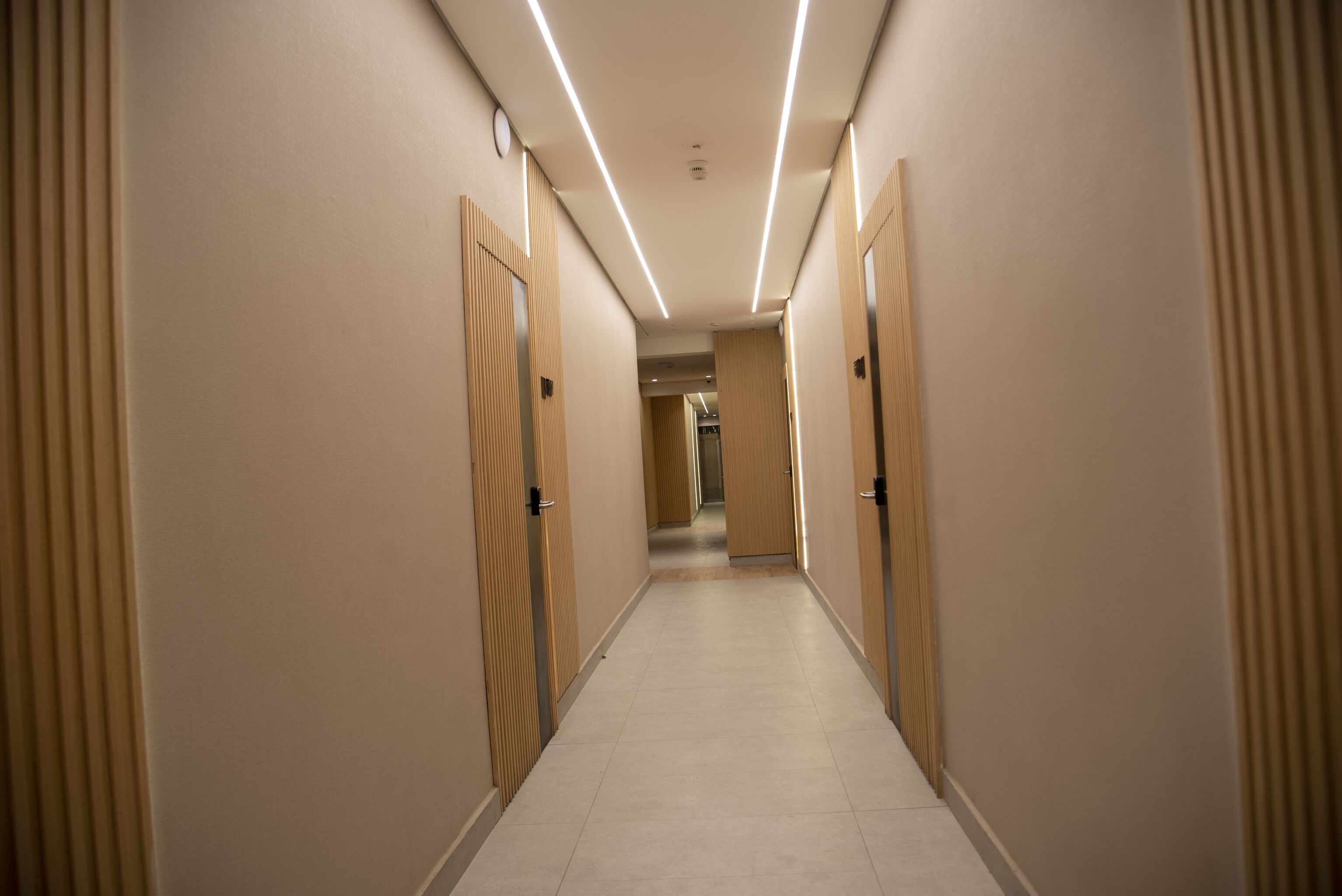 A hotel corridor with wooden doors, a tiled floor, and overhead lighting.