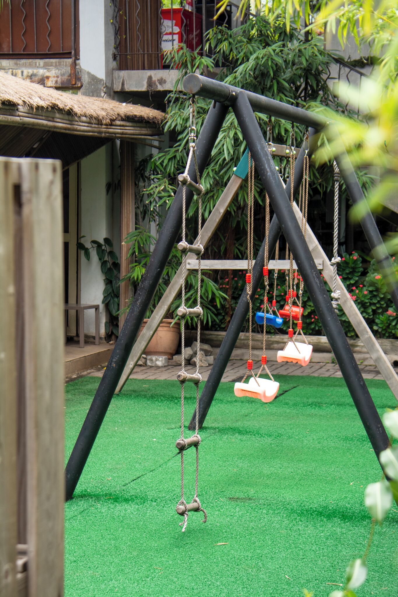 A wooden swing set with two swings, a rope ladder, and a green artificial turf ground.