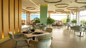 Un restaurante espacioso con numerosas mesas y sillas, amplios ventanales y plantas de interior.