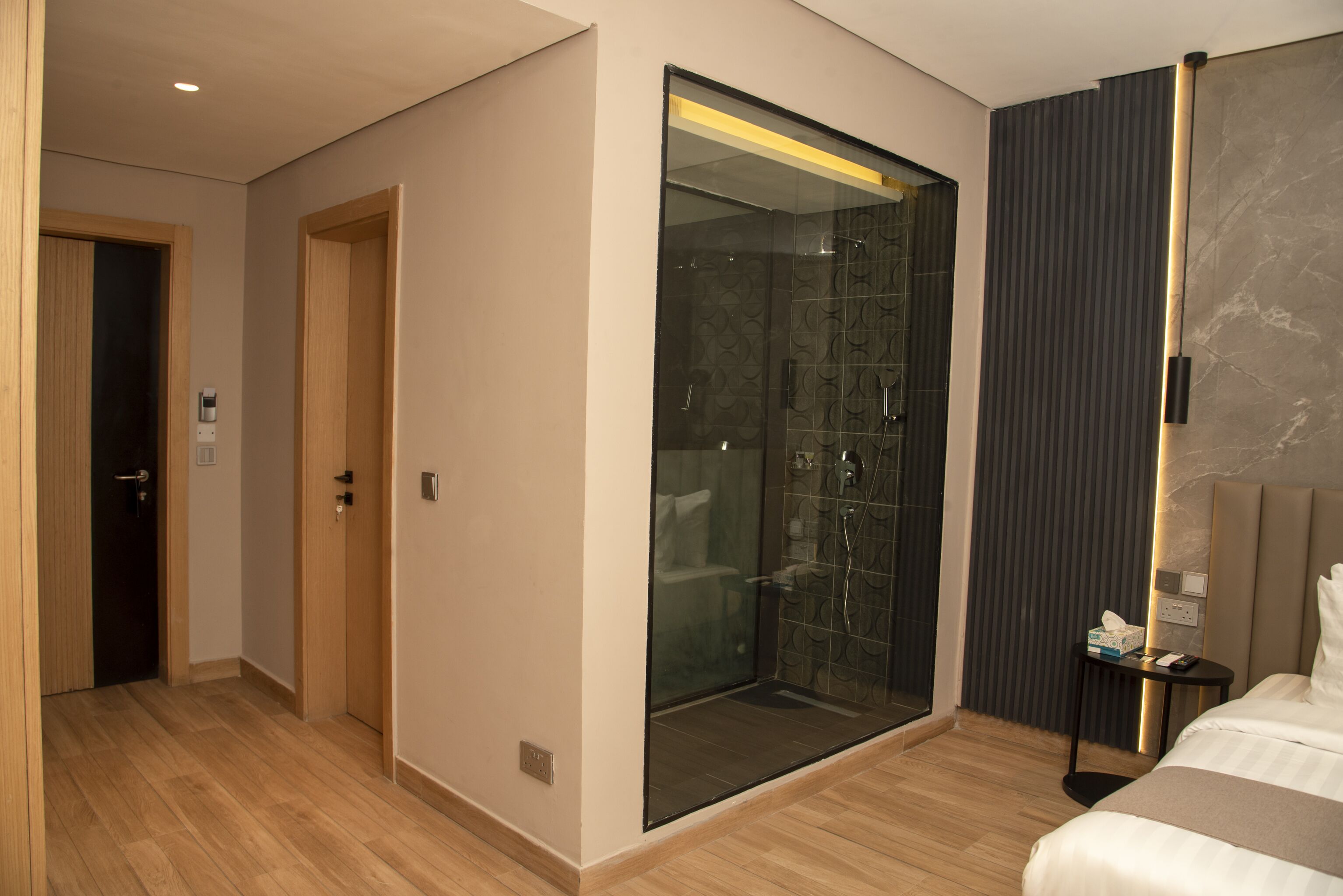 Ein modernes Hotelzimmer mit einer glasumrandeten Dusche, Holzboden und einem Bett mit Kopfteil.
