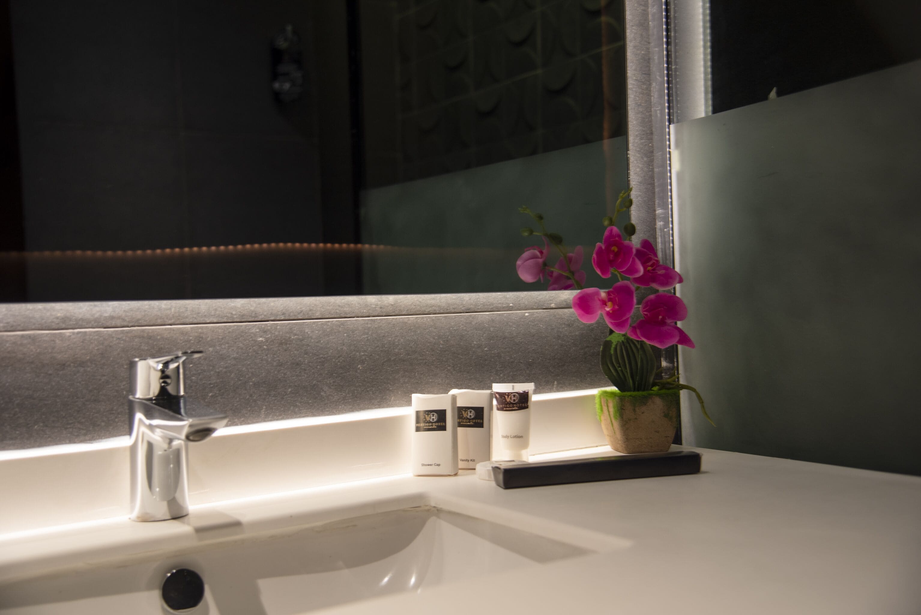 A bathroom sink with a mirror, a potted orchid, and three skincare products.