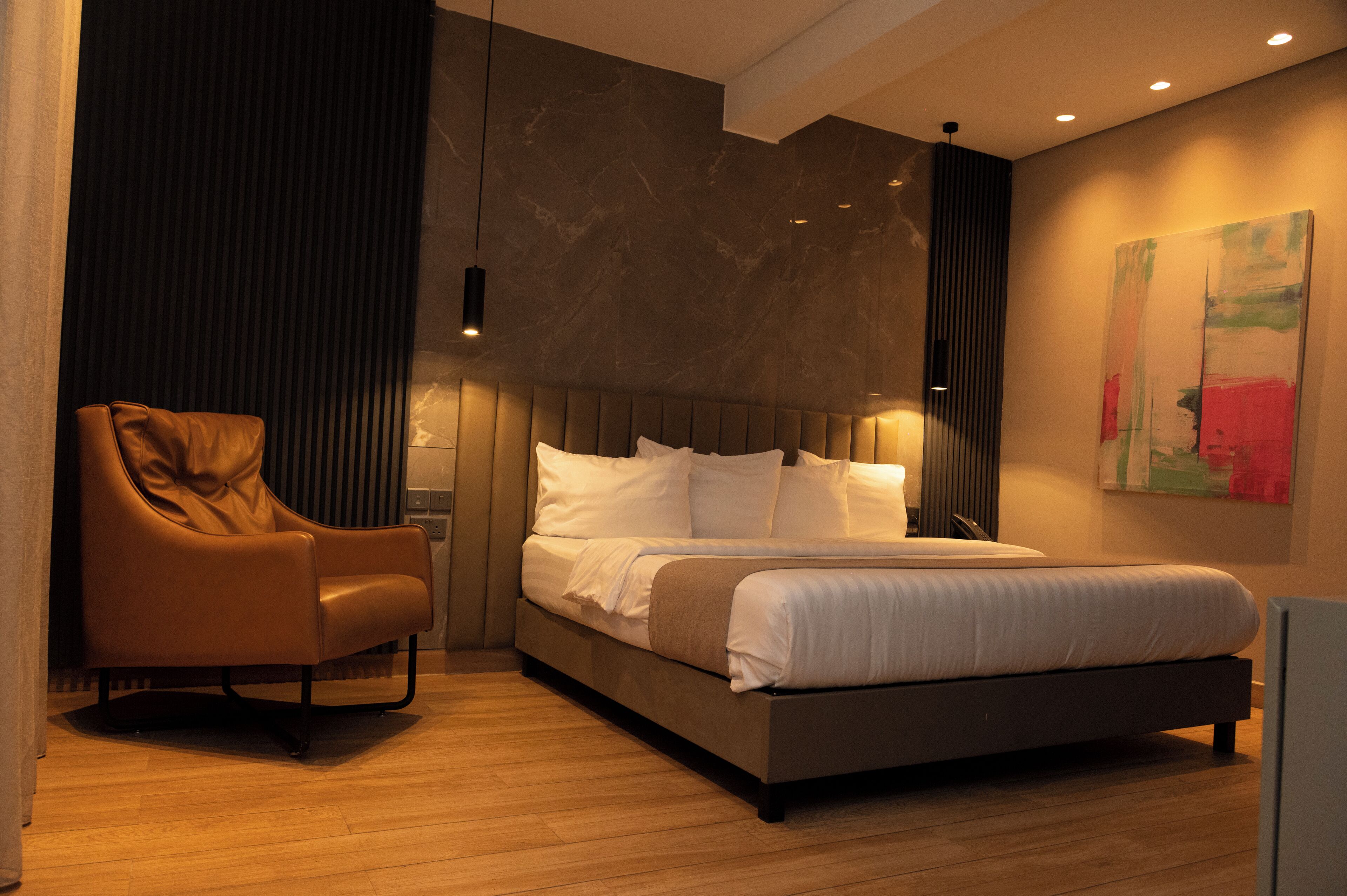A modern bedroom with a large bed, a leather armchair, and a minimalist decor.
