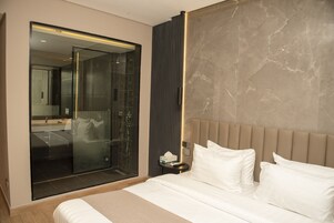 Habitación de hotel moderna con una cama grande, cabina de ducha de vidrio y una pared de acento de mármol.