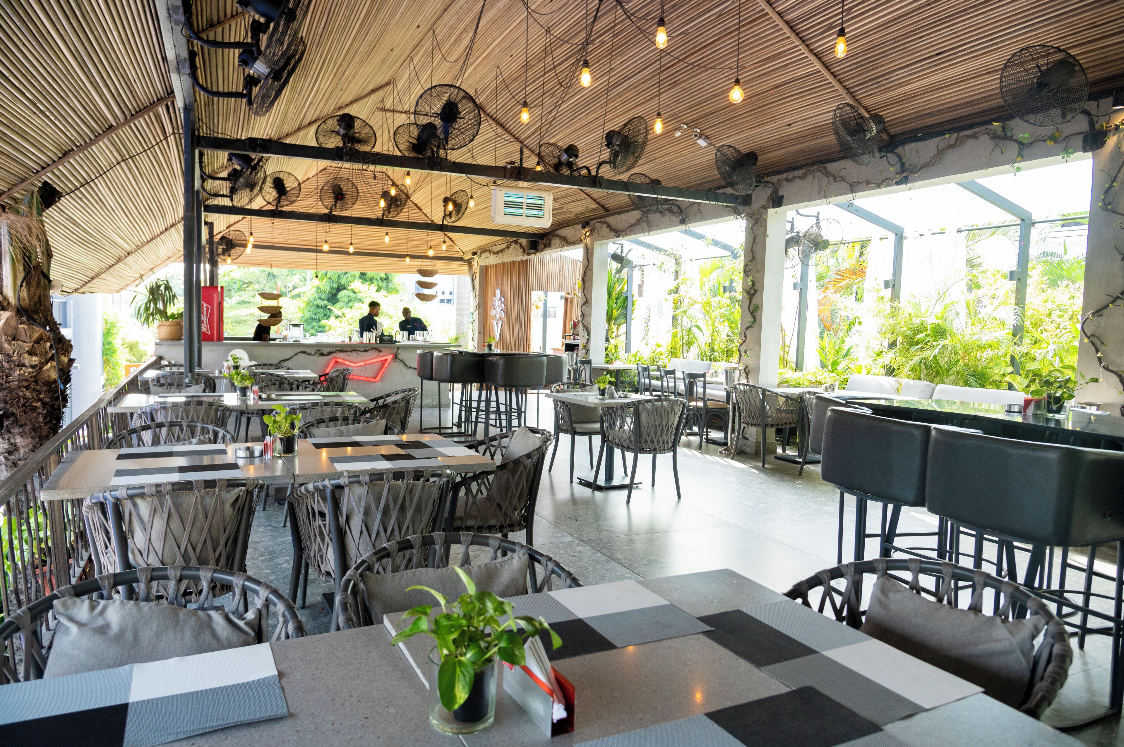 Un restaurante al aire libre con mesas a cuadros, sillas de mimbre y ventiladores en el techo.