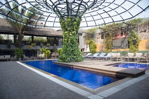 An indoor swimming pool with a glass ceiling, surrounded by lounge chairs and a tropical plant wall. - VERTIGO HOTEL (Lagos)