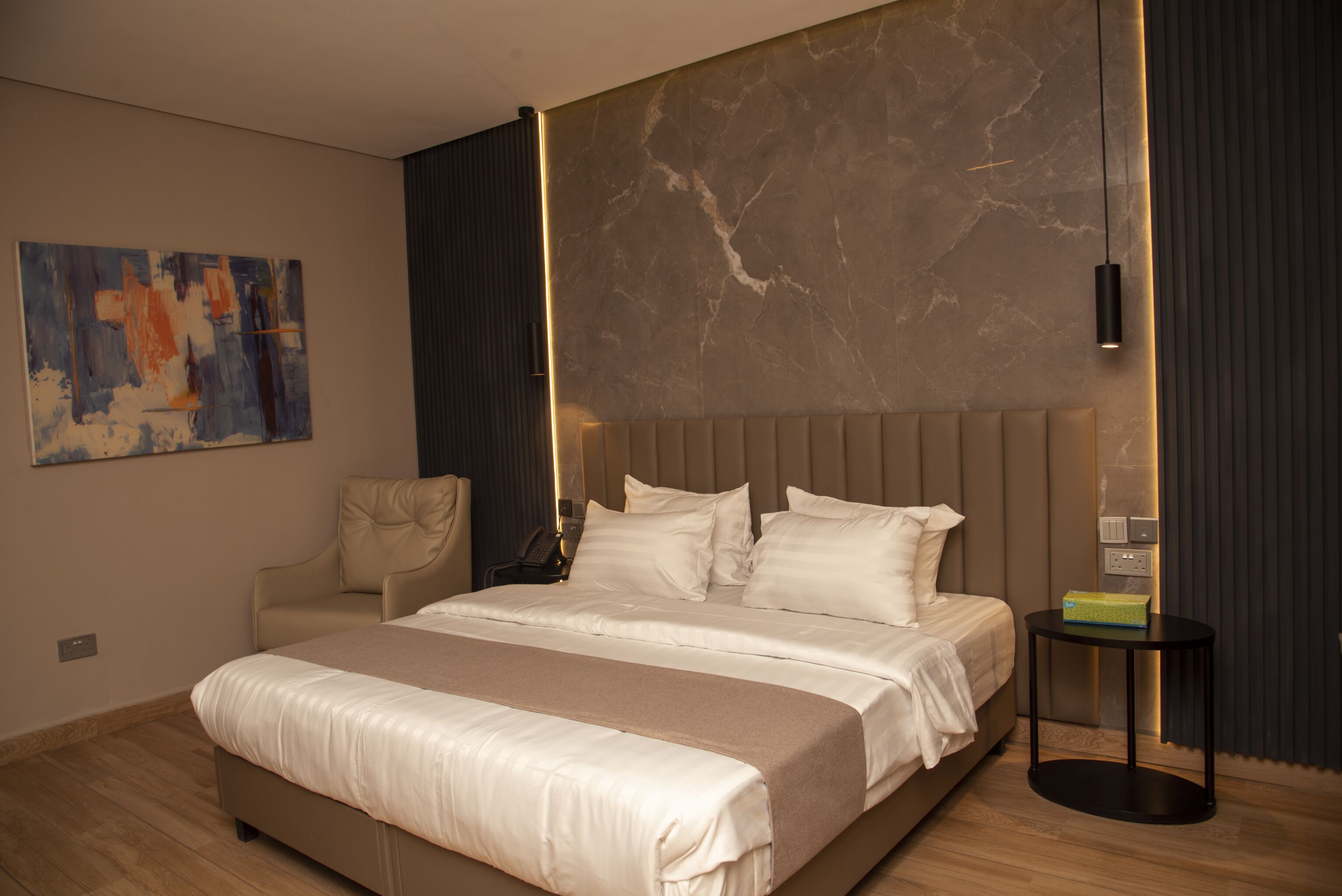 Un dormitorio moderno con una cama grande, cabecera, mesita de noche y una obra de arte colgada en la pared.