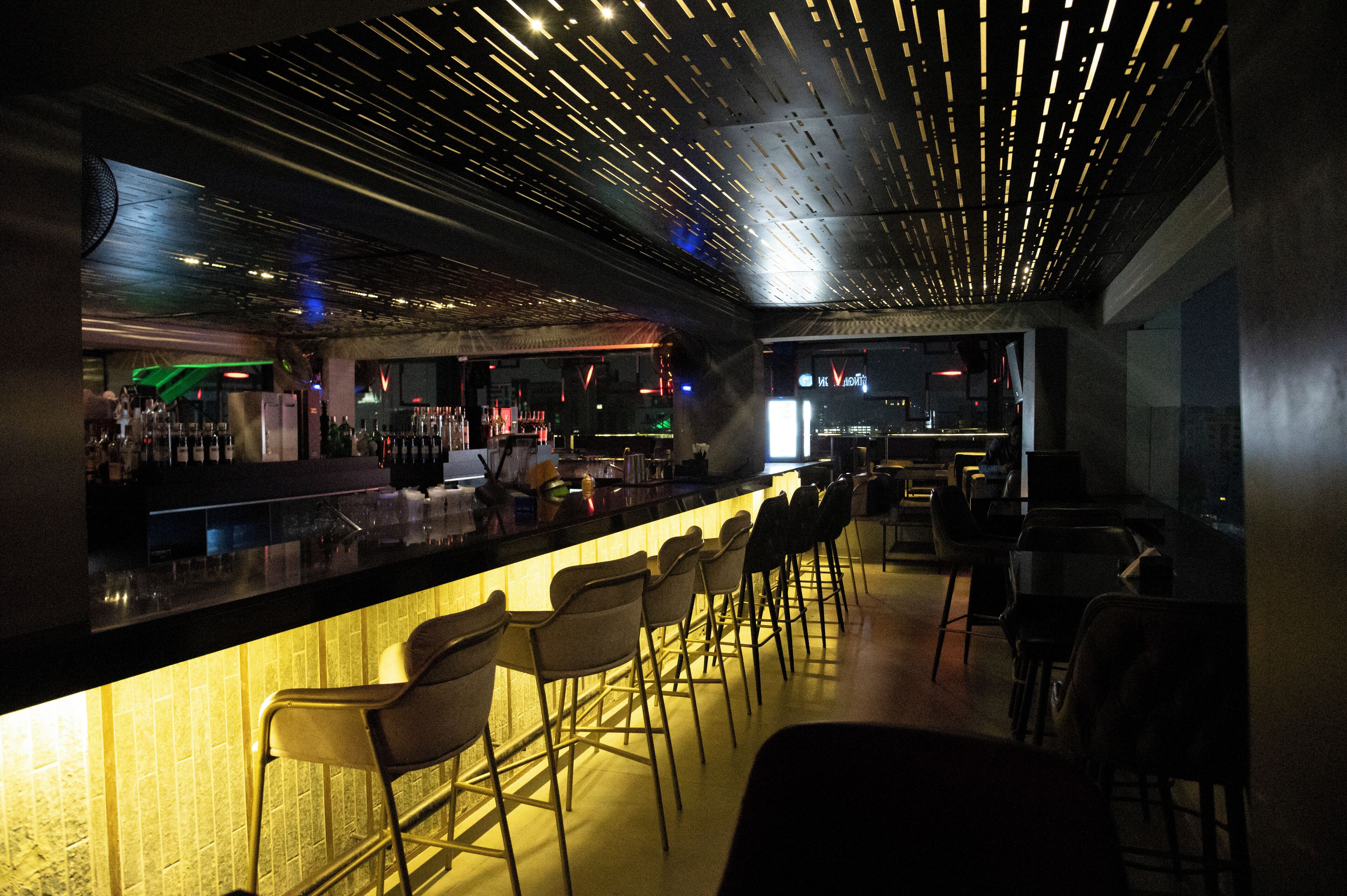 A bar area with a long counter, multiple bar stools, and a modern ceiling design.