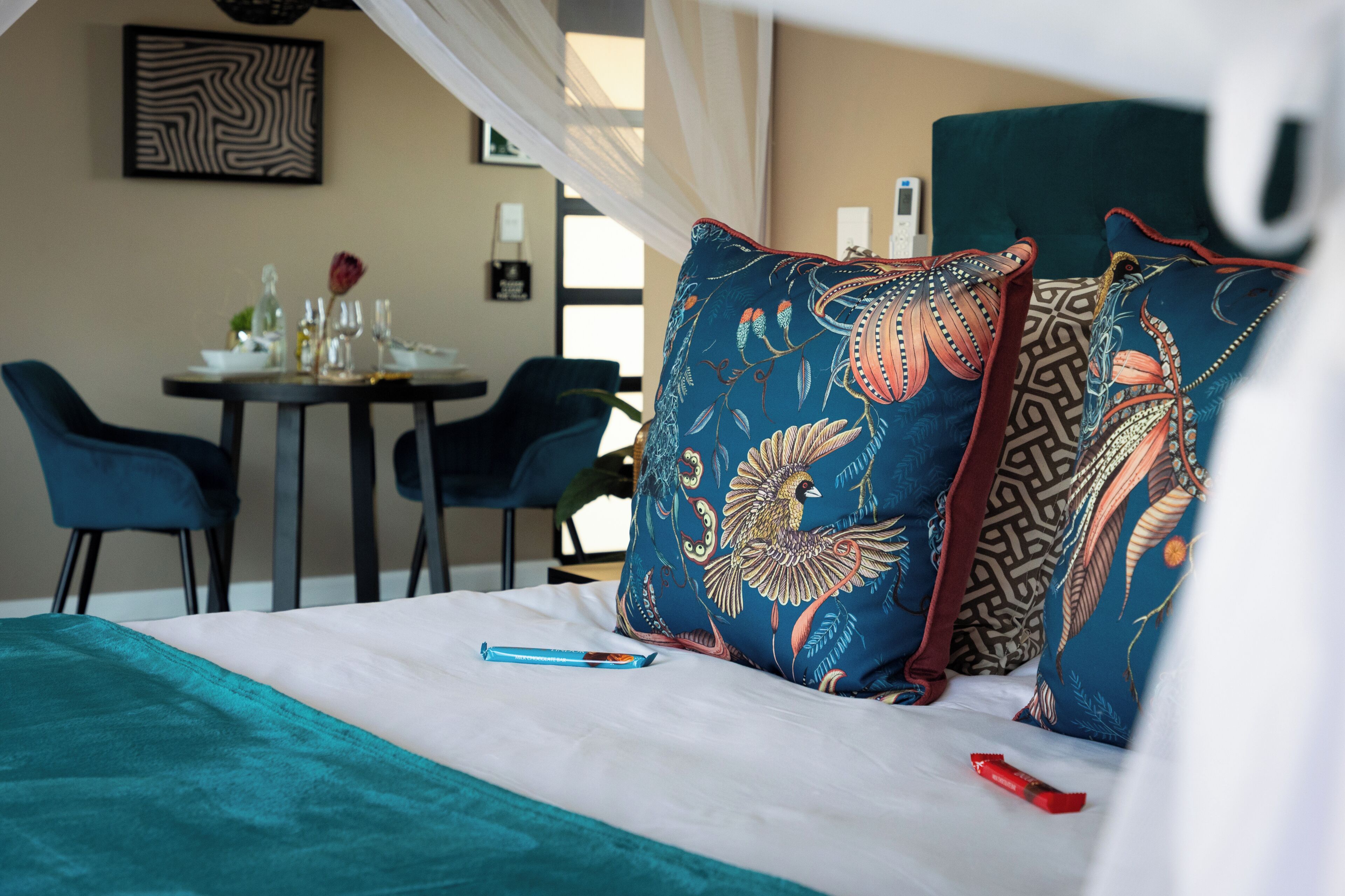 Una habitación de hotel con una cama, una mesa con sillas y un cojín decorativo con un diseño de pájaro.