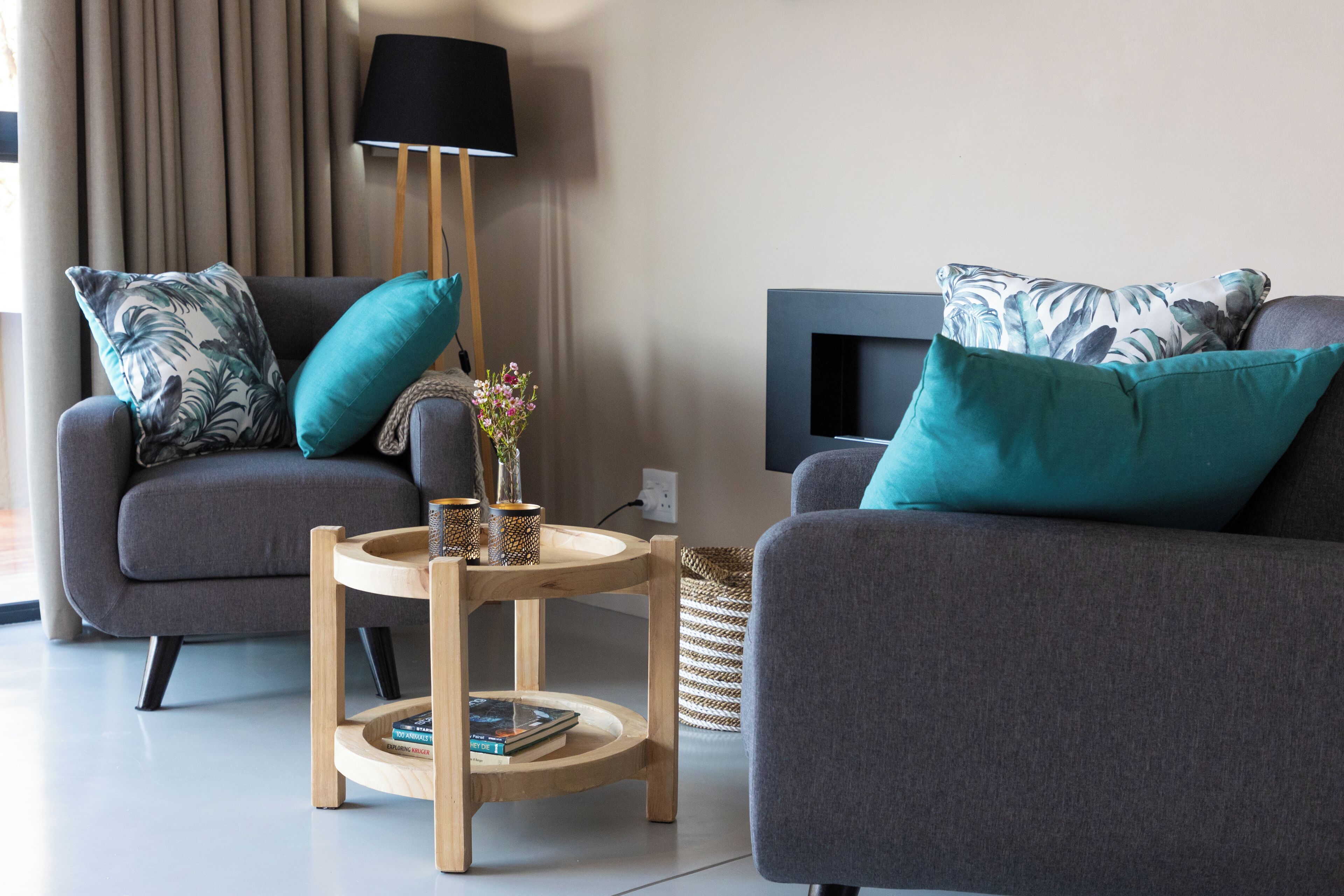 A modern living room with two grey sofas, a wooden side table, a black floor lamp, and a flat-screen TV mounted on the wall.