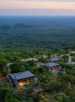 Un moderno resort con varias edificaciones rodeado de un bosque denso, que ofrece vistas panorámicas del paisaje.
