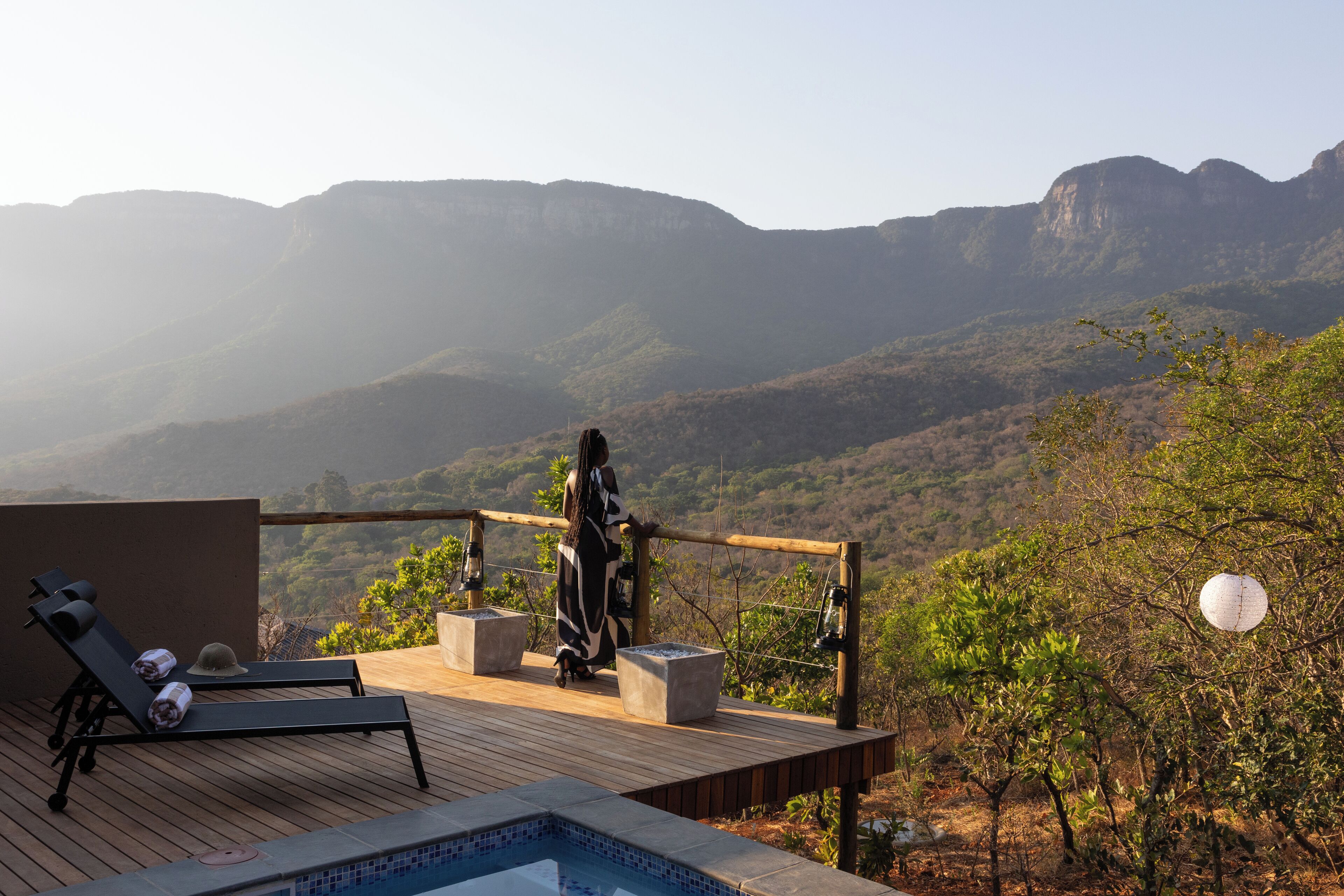 Terraza de madera con sillones de descanso y piscina, con vistas a un paisaje montañoso.