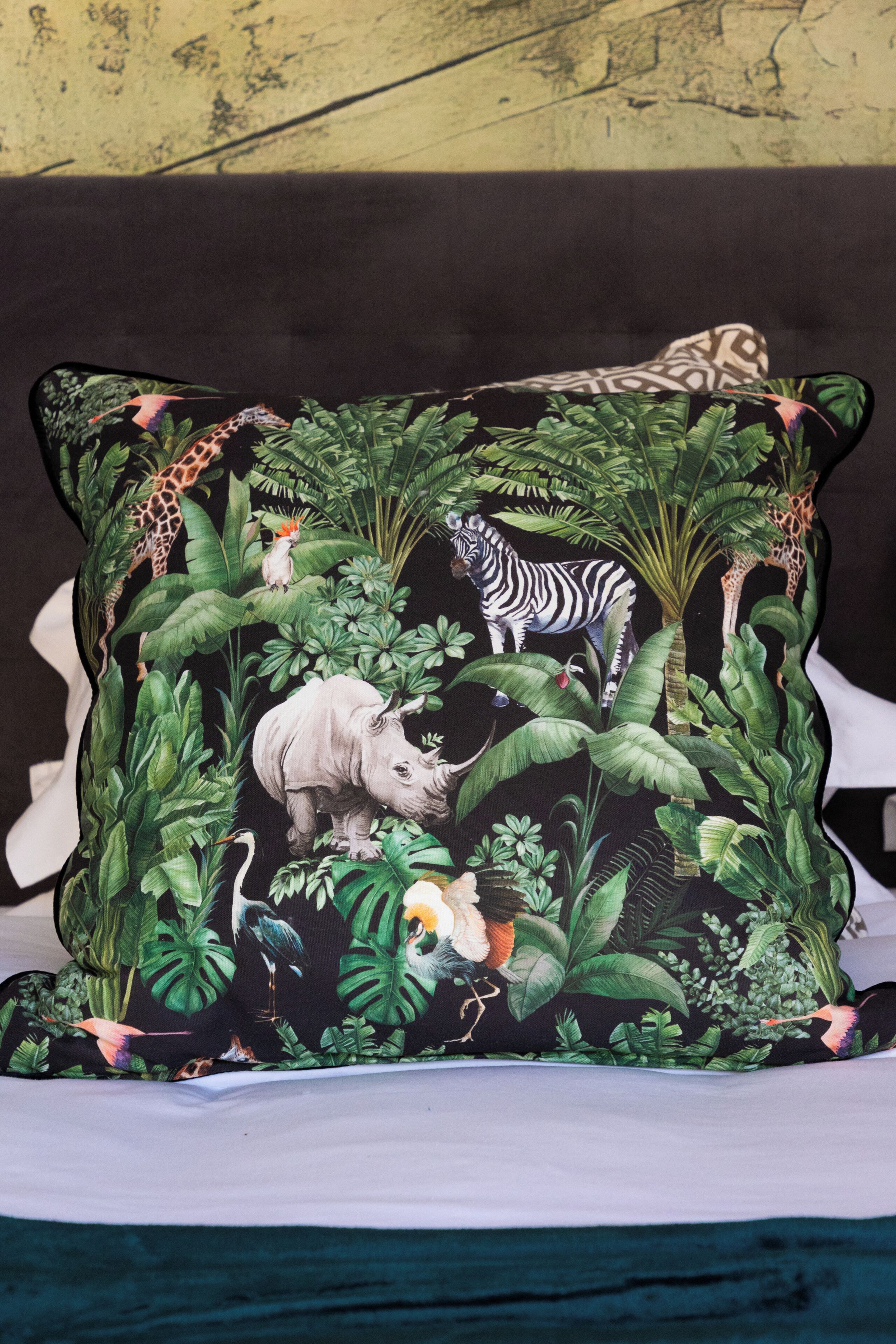 A pillow with a jungle-themed design featuring animals like a giraffe, zebra, and elephant.